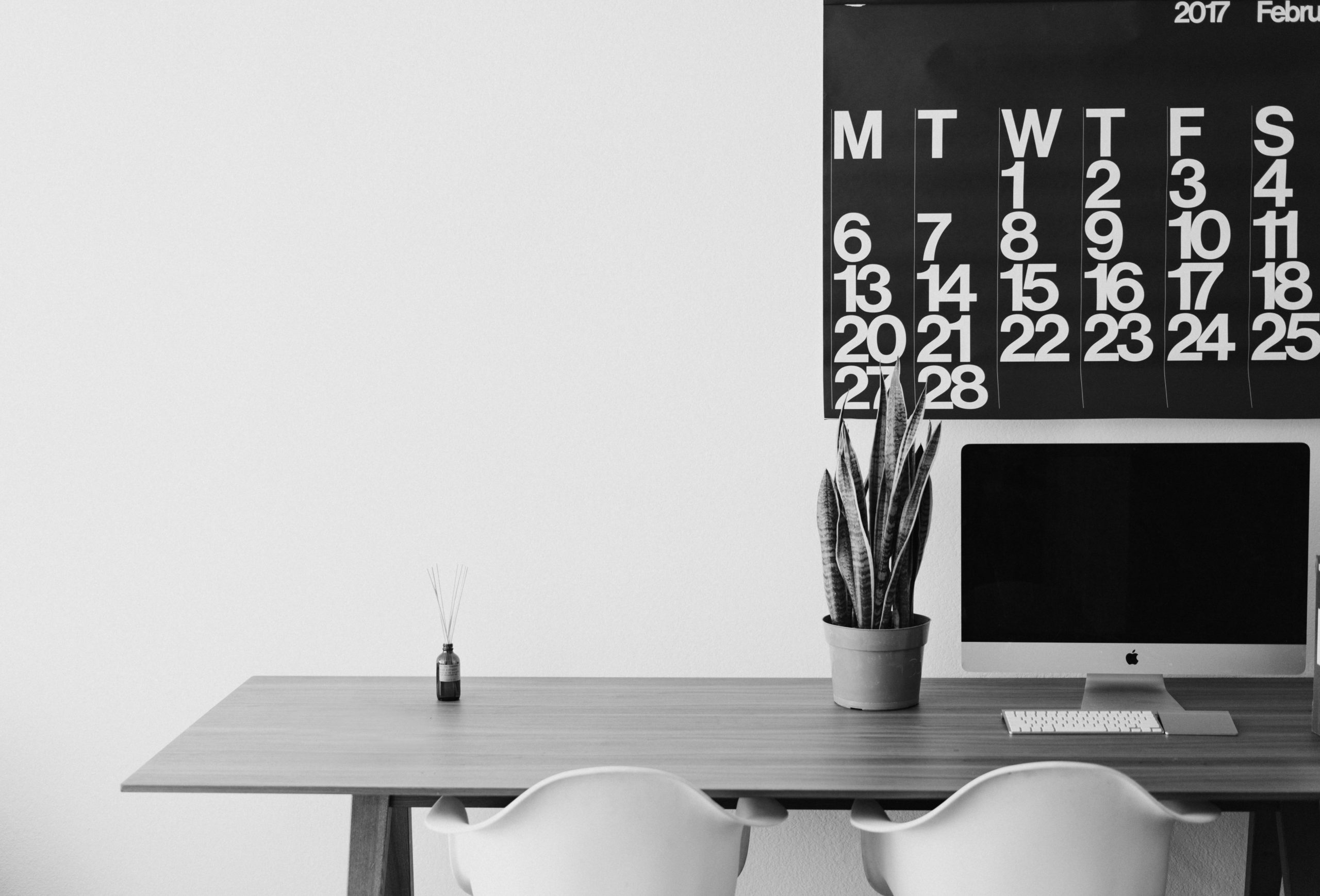 Black and white image of a minimalist desk with calendar on wall